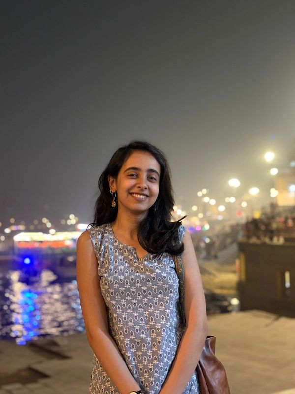 A young woman smiling by a waterfront at night with city lights in the background.