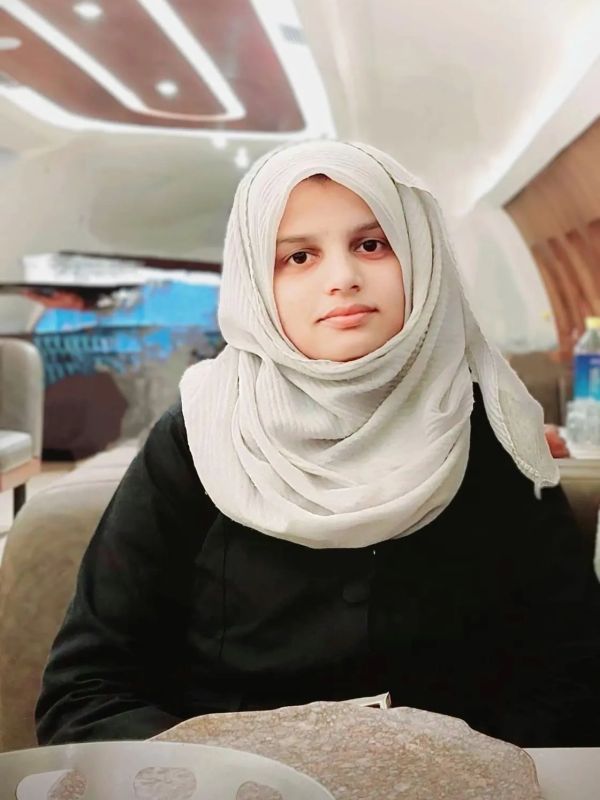 A woman wearing a white hijab and black outfit sitting indoors.