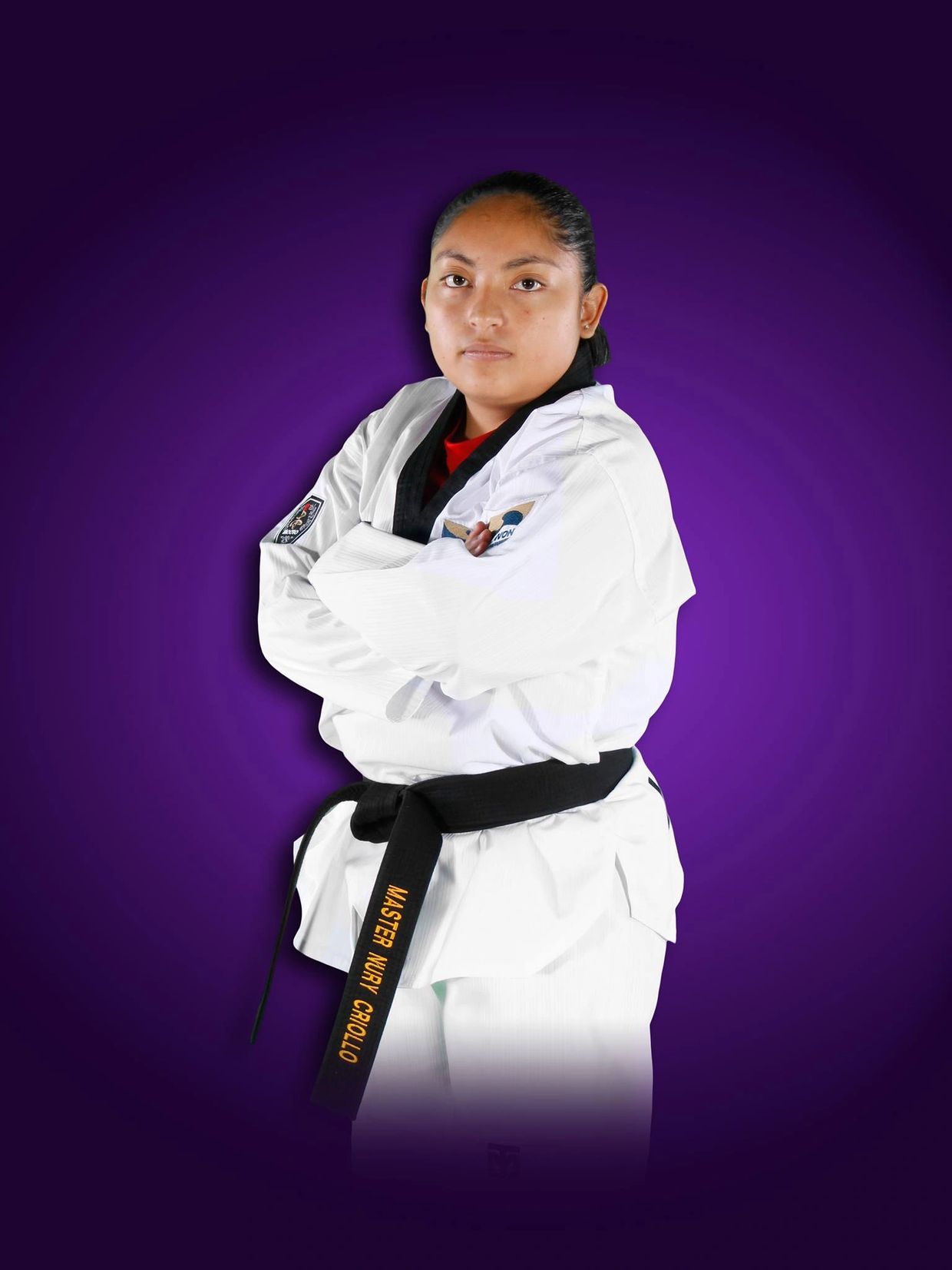Martial artist in white uniform with black belt, arms crossed, against a purple background.