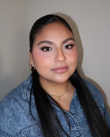 Young woman with long black hair wearing a denim shirt and gold earrings.
