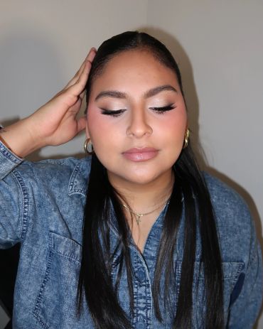 Woman with flawless makeup and sleek hair in a denim jacket.