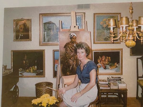 Woman artist sitting by her painting in an art-filled room.