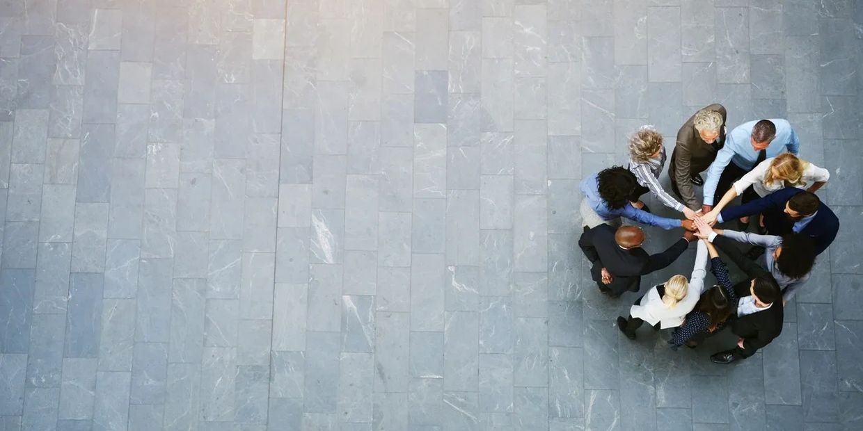 A diverse group joining hands in a teamwork circle on a tiled floor.