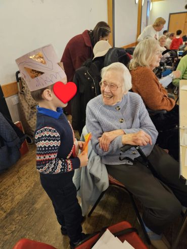 Young child interacting with smiling elderly woman in a social setting.