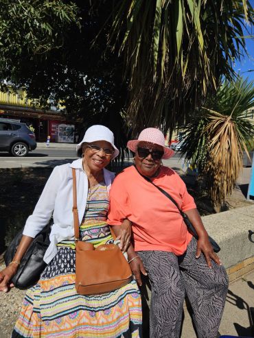 Two elderly women sitting outdoors wearing hats.