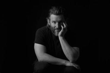 Man with beard resting his face on his hand in black and white.