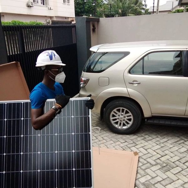 Man in safety gear carrying a solar panel outdoors near a vehicle.