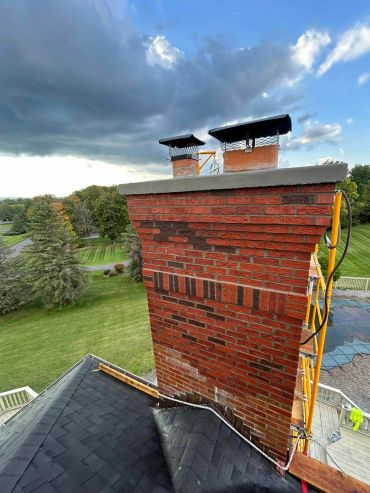 Tall red brick chimney on a roof with dramatic sky.