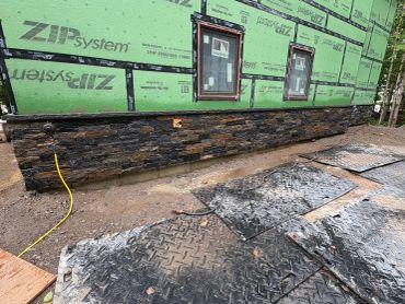 New house construction with stone siding and green sheathing.