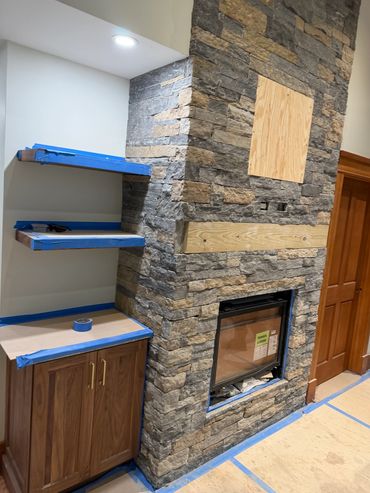 Stone fireplace with wooden shelves and cabinets under construction.