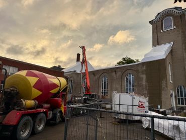 Concrete truck and construction equipment by church at sunset.