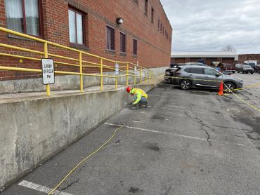 Worker measuring beside a brick building in a parking lot.