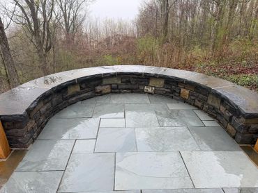 Curved stone bench with tiled floor in a natural setting.