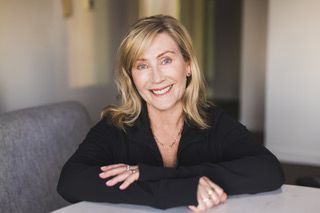 Smiling woman with blonde hair in black outfit.
