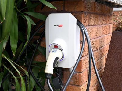 A SolarEdge electric vehicle charger mounted on a brick wall with a plugged-in charging cable.