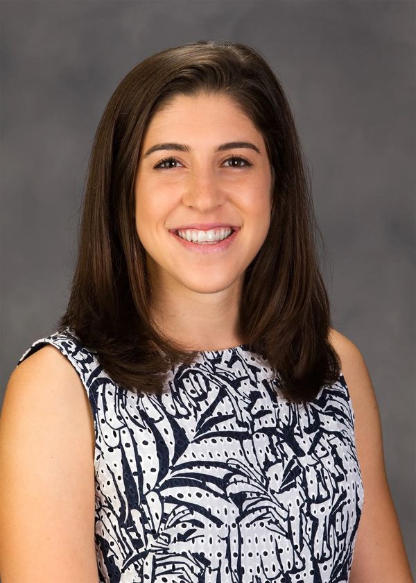 Smiling woman in a patterned sleeveless top against a gray background.