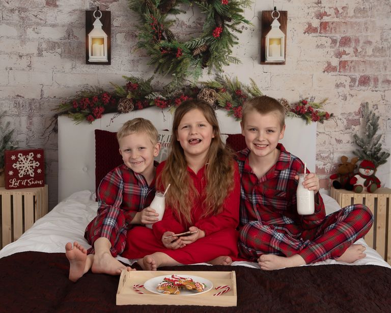 3 children sitting on a holiday themed bed and having a snack of milk and cookies
