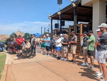 A group of people standing in a line outdoors listening to a speaker.