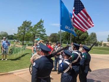 Color guard members hold flags during a public event on a sunny day.