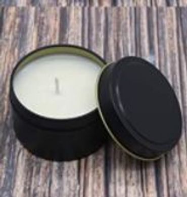 opened  soy candle tin with lid leaning against the soy candle sitting on a table