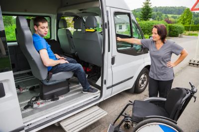 Young man sitting in accessible van with woman and wheelchair outside.