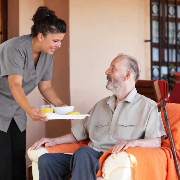 Caregiver serving breakfast to an elderly man.