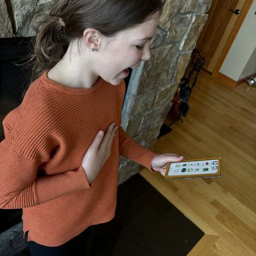 A girl in an orange sweater excitedly looking at her phone indoors.
