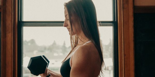 Woman lifting a dumbbell by a window in workout attire.