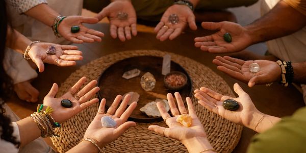 Hands holding various crystals in a circle around a tray.