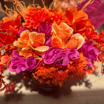 Vibrant orange and purple artificial flower bouquet in warm light.