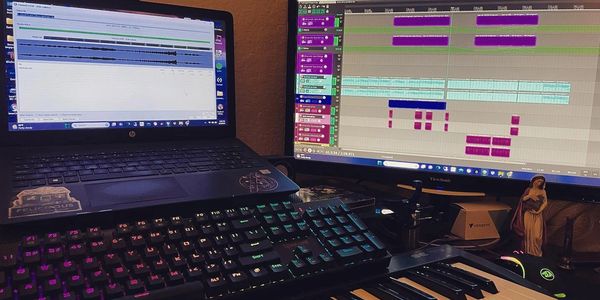 A music production setup with dual monitors, keyboard, and MIDI controller.
