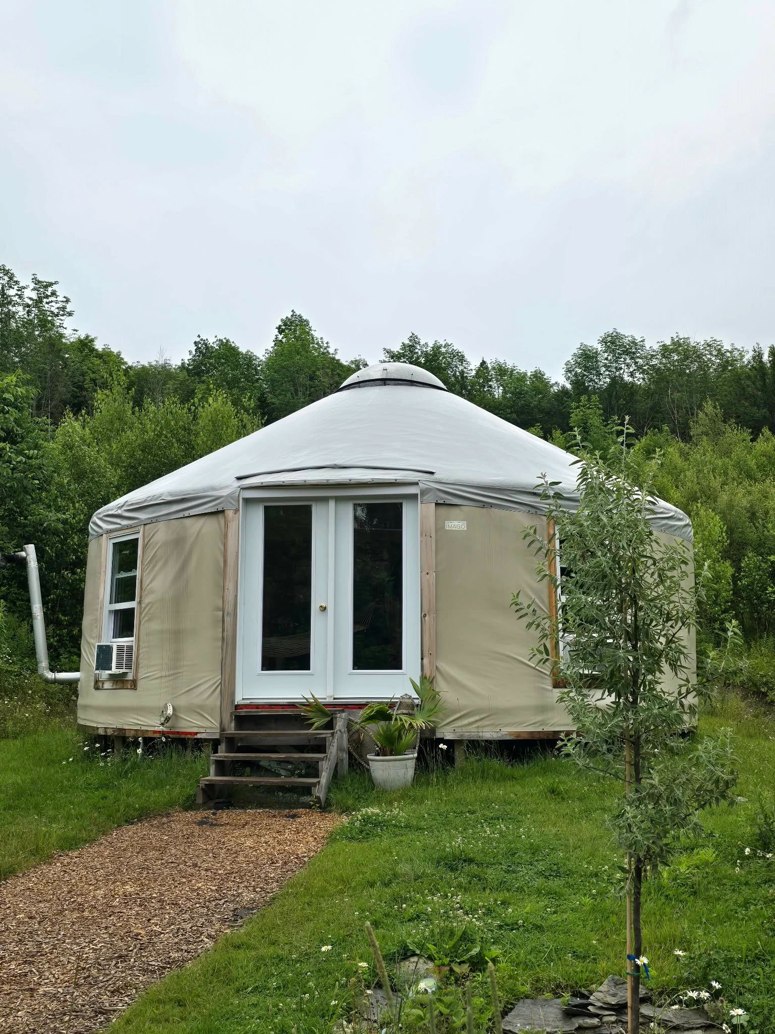 Round yurt with beige and white exterior in greenery.