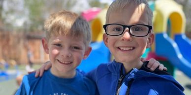 Two boys smiling outdoors with playground slides in the background.