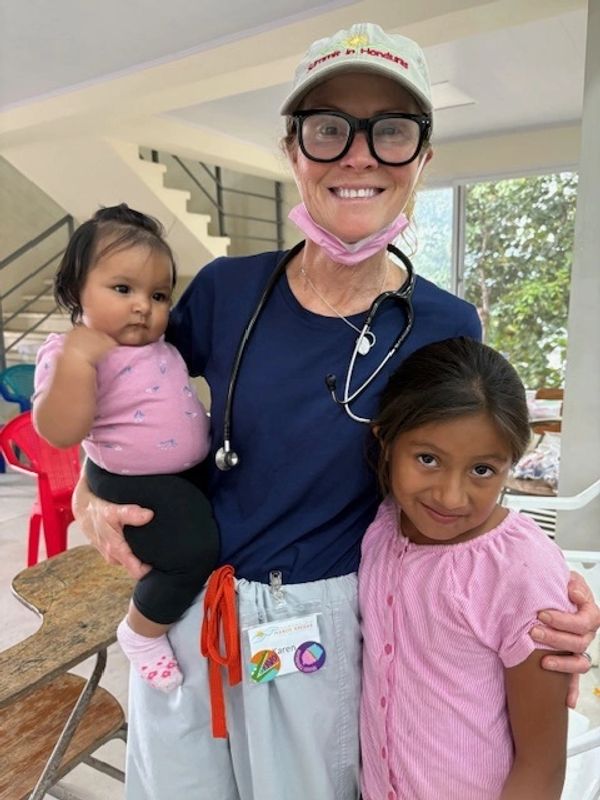 A smiling healthcare worker with two children indoors, showing care and warmth.