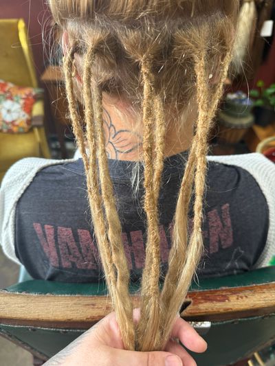 Person with freshly made dreadlocks being held up.