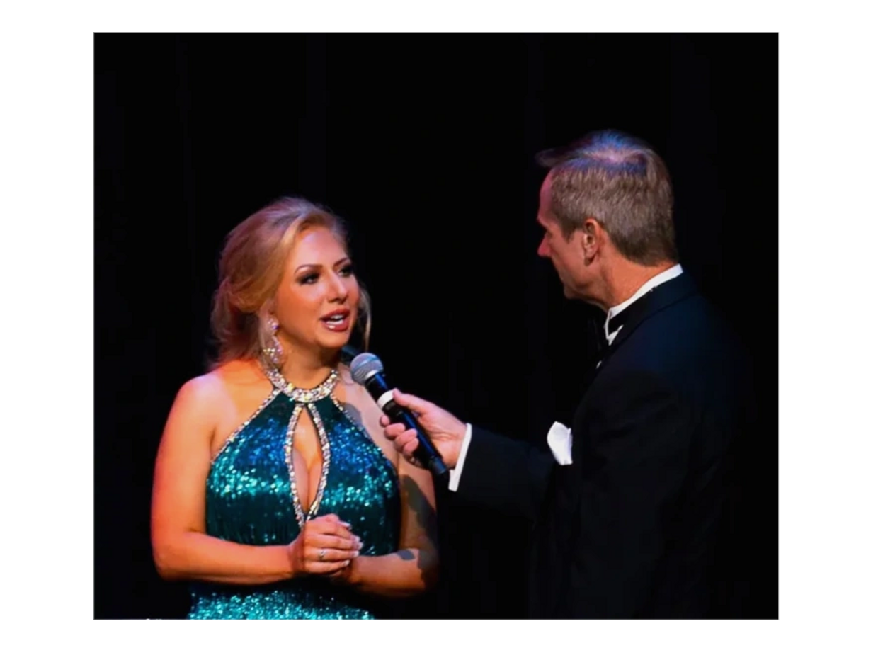 Woman in a sparkling teal gown being interviewed on stage.