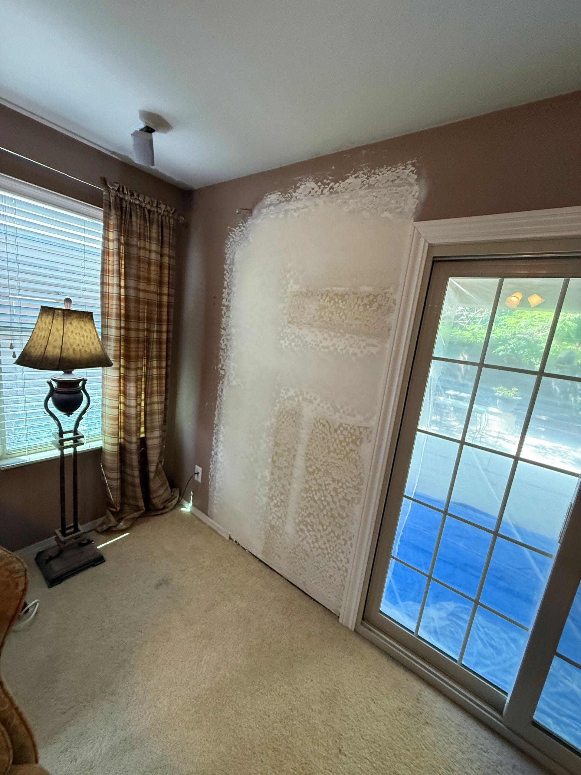 Room wall partially repainted near sliding glass door and window with lamp.