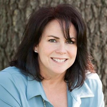 Smiling woman with dark hair outdoors against a tree background.