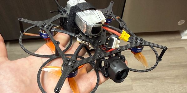 Hand holding a small racing drone with orange propellers.