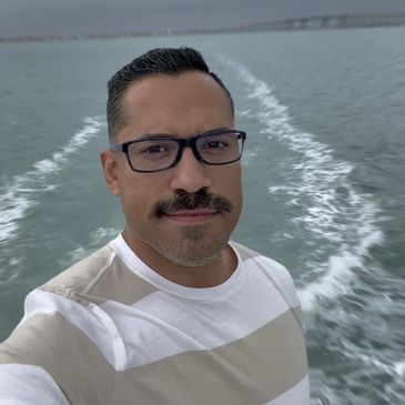 Man with glasses and mustache on a boat, water in the background.