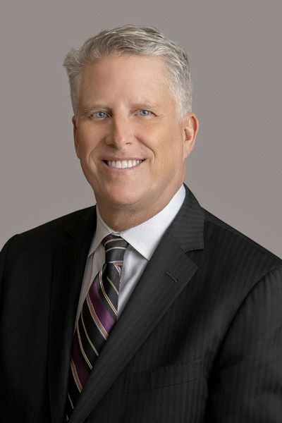 Professional middle-aged man in suit with striped tie smiling against gray background.