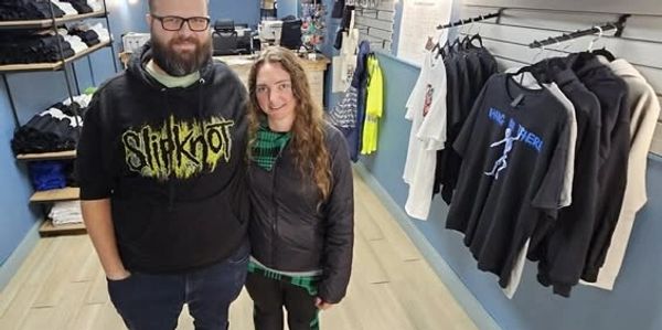 A man and woman standing in a clothing store with various shirts and merchandise.
