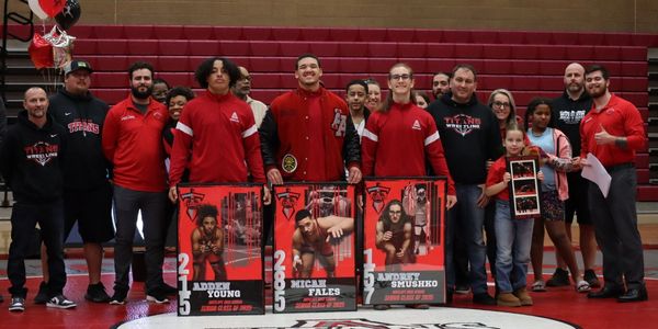 High school wrestling team celebrating senior athletes with posters in gym.