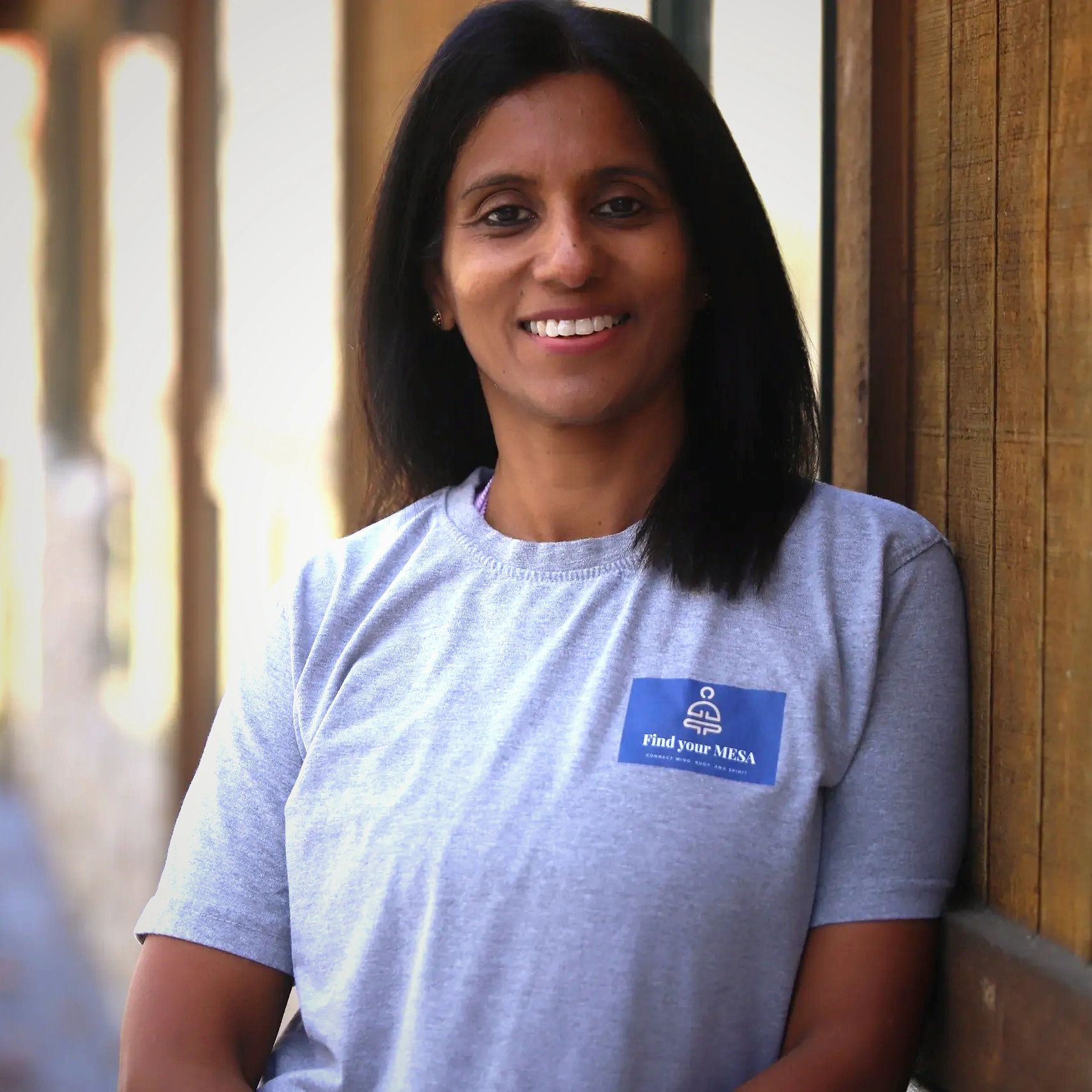 Woman smiling in a gray shirt with a wooden background.