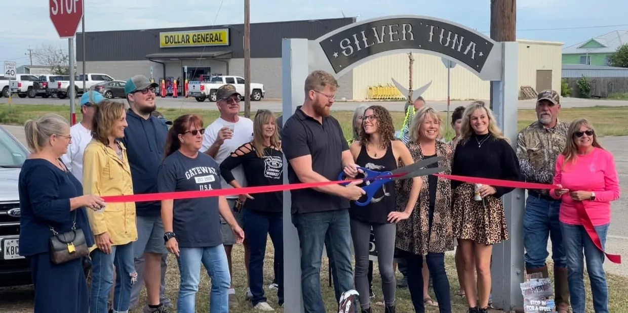 Group of people at a ribbon-cutting ceremony in front of a sign saying Silver Tuna.