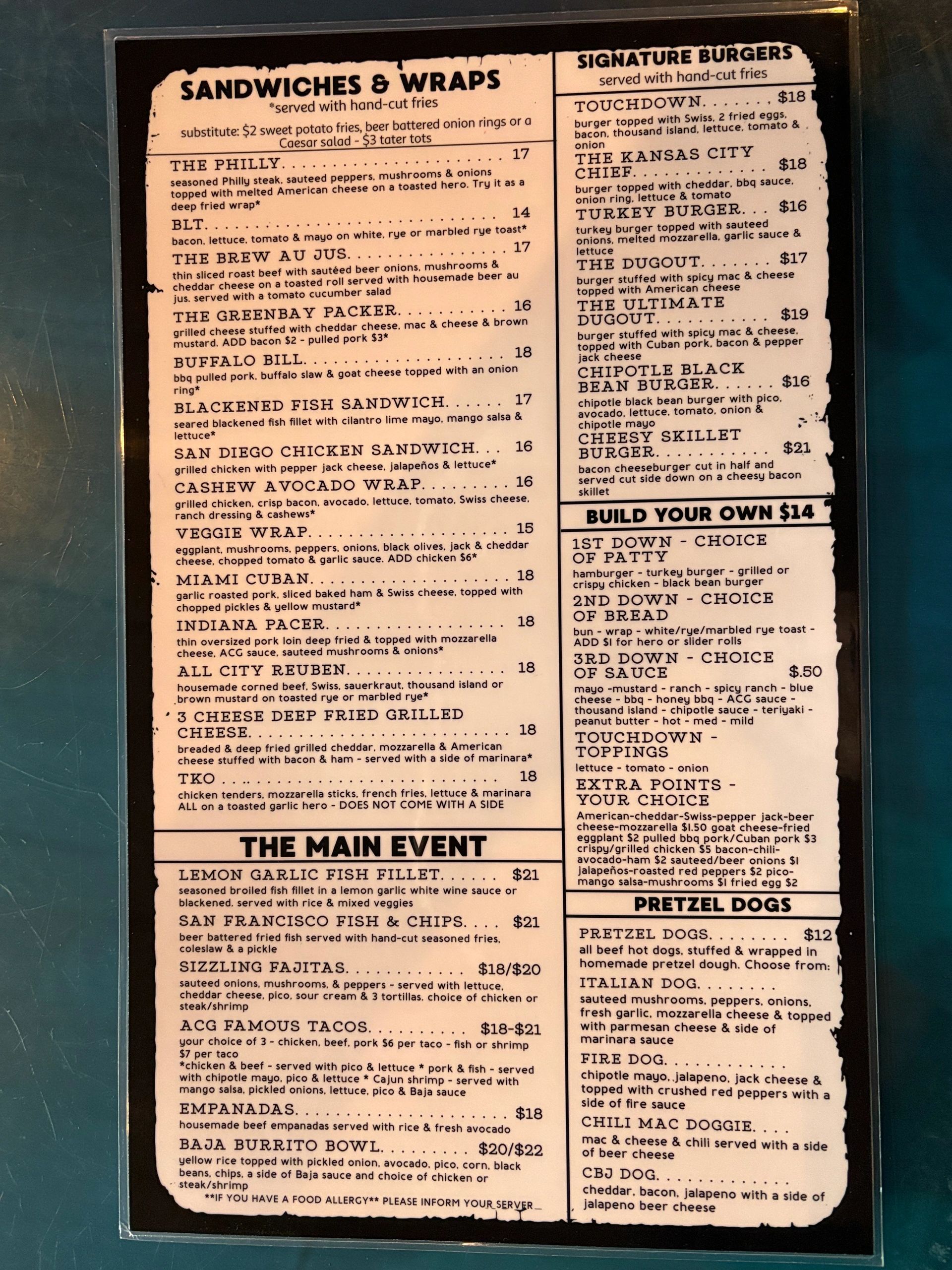 Menu featuring sandwiches, wraps, signature burgers, fish dishes, and pretzel dogs with detailed descriptions and prices.