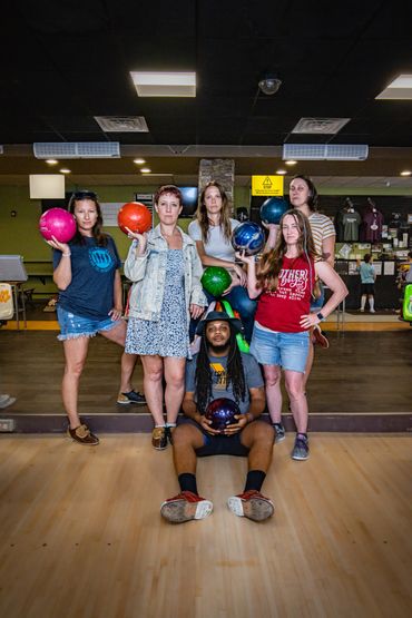 People in a bowling alley, holding bowling balls and looking at the camera.