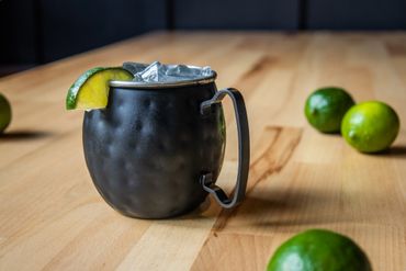 A Moscow Mule surrounded by limes on a wooden table.