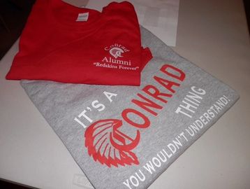 Two folded shirts, one red alumni and one gray with a Conrad design.