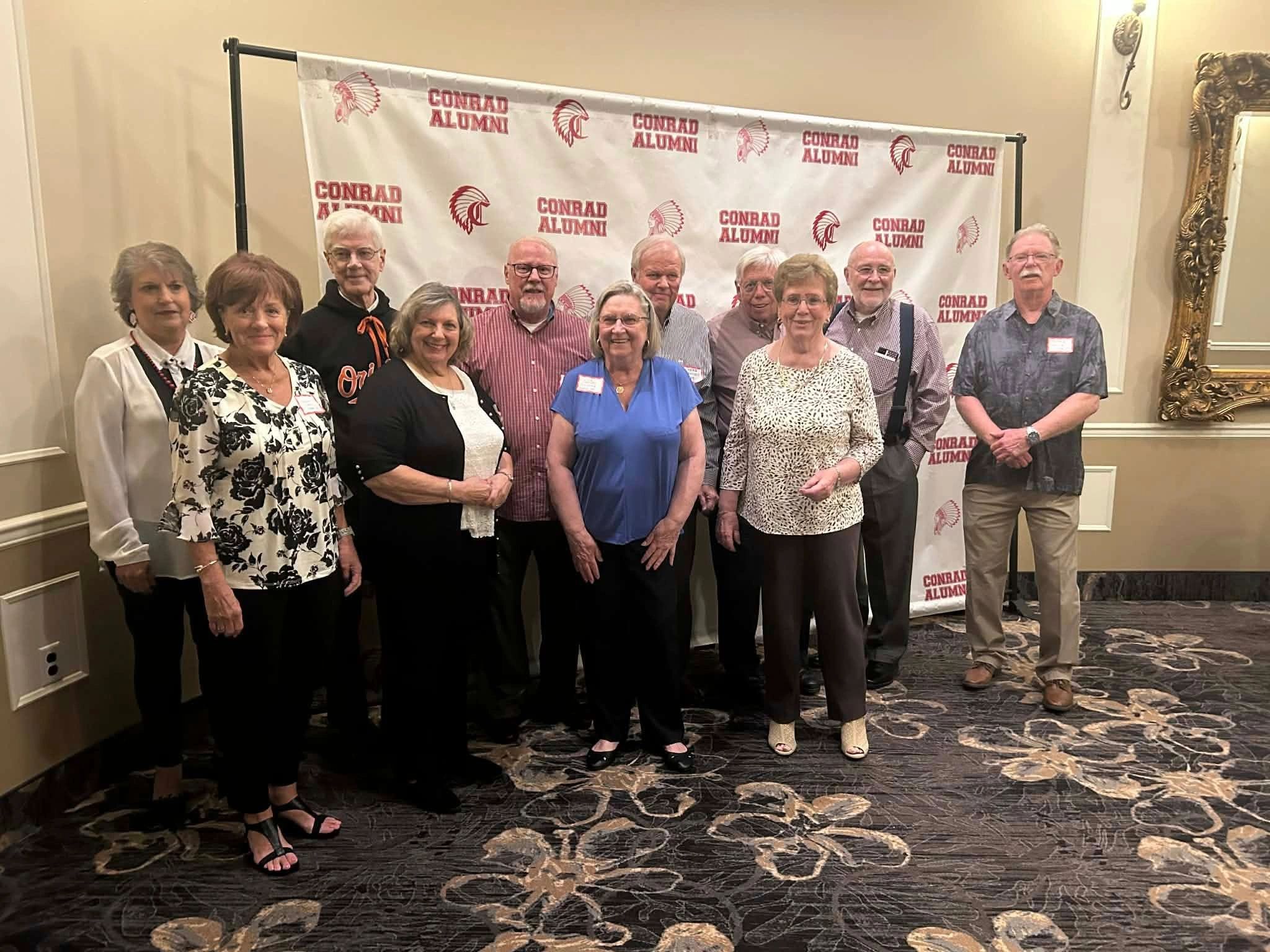 Group of alumni posing in front of a Conrad Alumni backdrop.